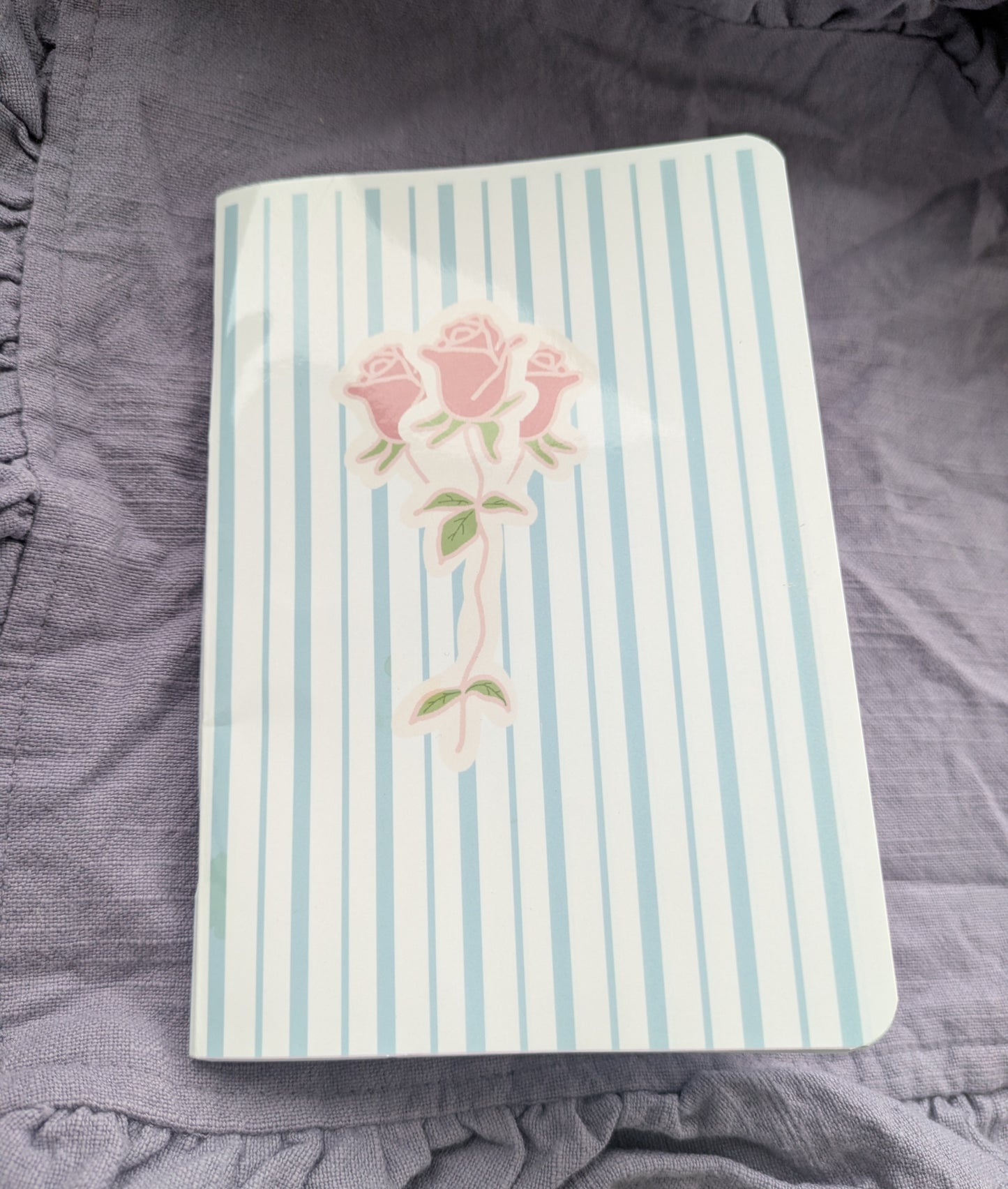 Notebook with pink roses on a striped cover, placed on a textured surface.